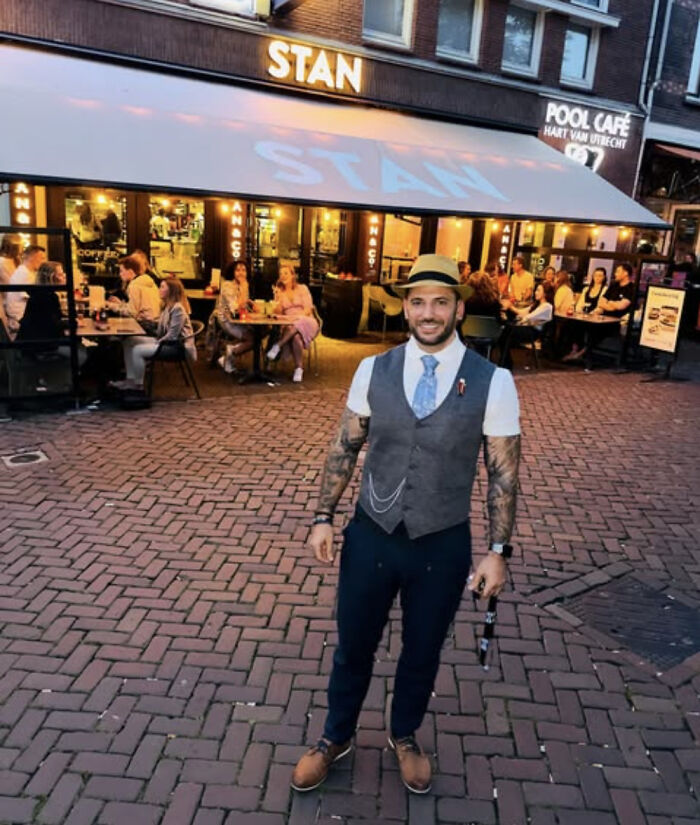 Man with tattoos wearing vest and hat standing outside Stan cafe with diners in the background, Harry Potter star Viktor Krum news. Man with tattoos wearing vest and hat standing outside Stan cafe with diners in the background, Harry Potter star Viktor Krum news.