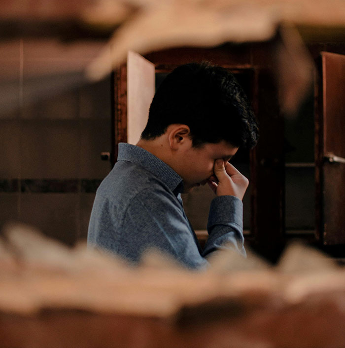 Man in a blue shirt showing stress and regret, illustrating huge risks taken for no logical reason in a dimly lit room.