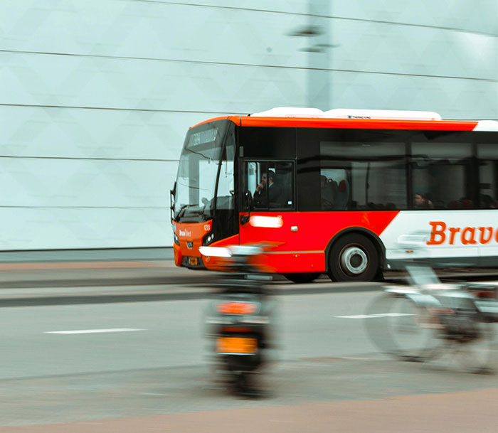 Red and white city bus moving fast on urban road, illustrating people taking huge risks with no logical reason.