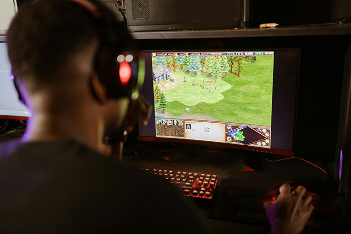 Person gaming on a PC with headset, taking huge risks in an intense strategy game session at night.