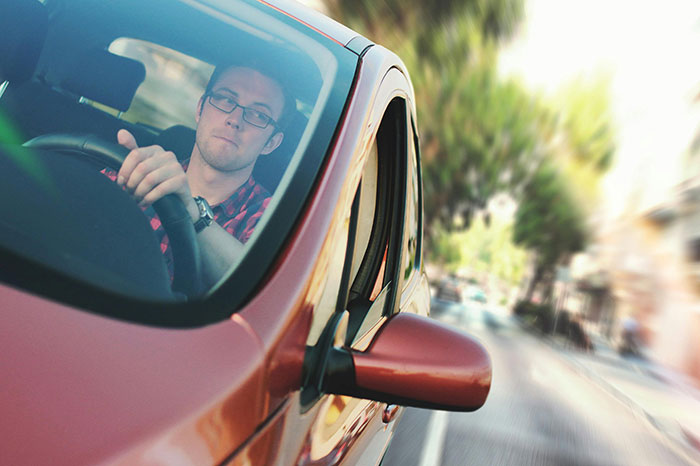 Young man taking huge risks driving a red car on a busy street with blurred motion for no logical reason at all