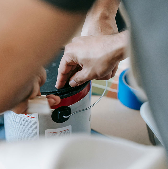 Hands opening a paint can showing a risky action with no logical reason in a close-up photo.