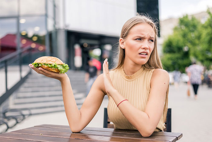Young woman showing dissatisfaction while holding a sandwich outdoors, depicting a highly sensitive reaction to high demands. Young woman showing dissatisfaction while holding a sandwich outdoors, depicting a highly sensitive reaction to high demands.