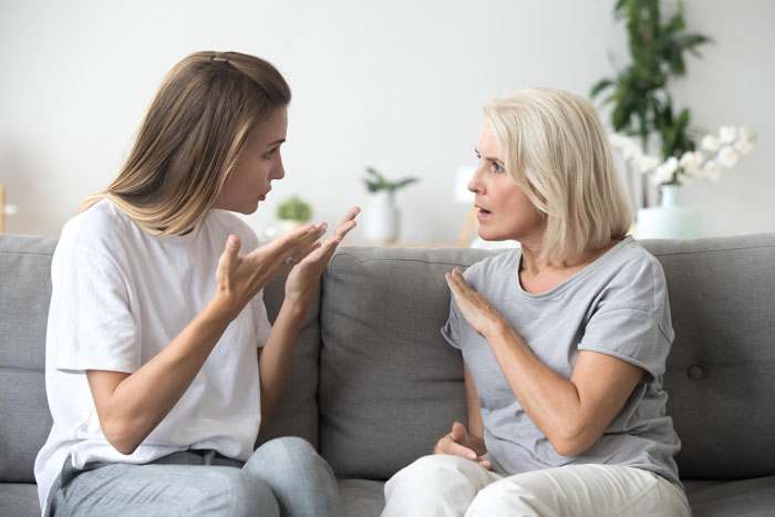 Woman and older woman arguing on couch about chores and sexist parents at home in a modern living room setting. Woman and older woman arguing on couch about chores and sexist parents at home in a modern living room setting.