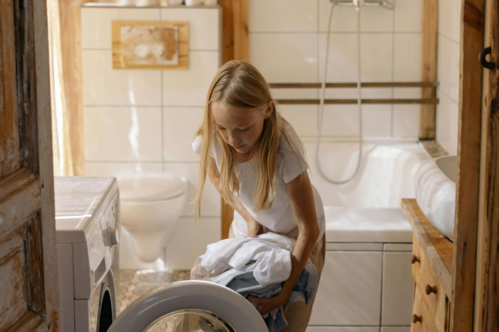 Young woman doing laundry in a bathroom, boycotting chores until her bros help clean in a sexist household. Young woman doing laundry in a bathroom, boycotting chores until her bros help clean in a sexist household.