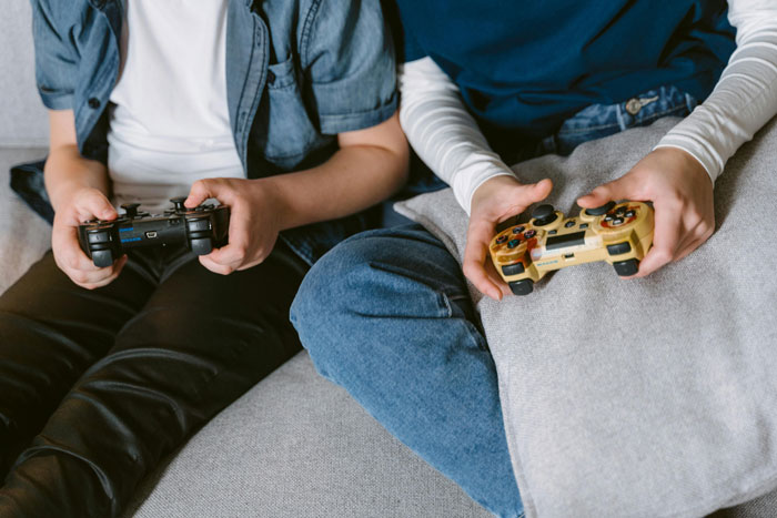 Two young men sitting on a couch playing video games, highlighting bros helping clean and chores conflict.