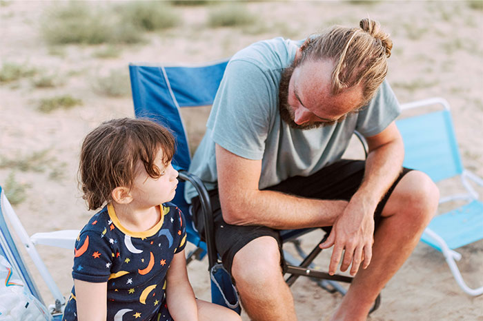 Dad sitting outdoors with child, discussing kids’ diet and custody issues at the beach in casual summer clothes. Dad sitting outdoors with child, discussing kids’ diet and custody issues at the beach in casual summer clothes.