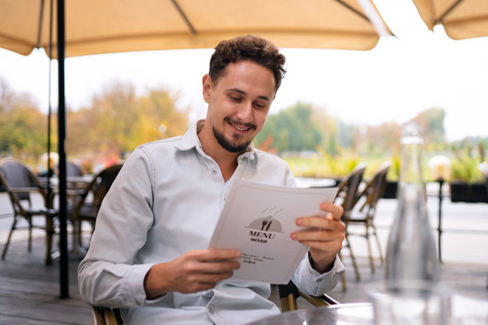 Man smiling while reading a menu at an outdoor restaurant, relating to friend laughs off vegan warning story. Man smiling while reading a menu at an outdoor restaurant, relating to friend laughs off vegan warning story.