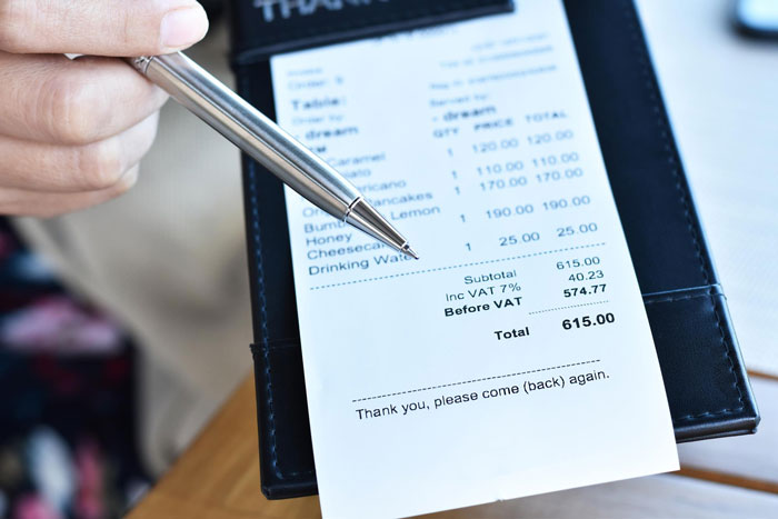 Hand pointing with pen at restaurant bill showing total amount, highlighting friend laughs off vegan paying only for food concept. Hand pointing with pen at restaurant bill showing total amount, highlighting friend laughs off vegan paying only for food concept.
