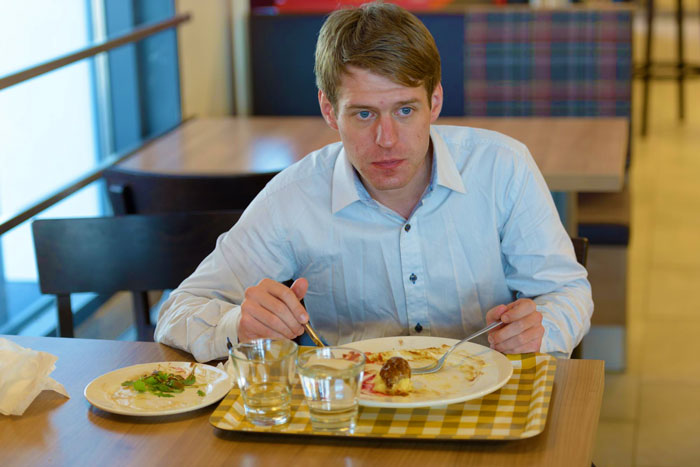 Young man eating alone in a restaurant, reflecting on the vegan’s warning about paying only for his food Young man eating alone in a restaurant, reflecting on the vegan’s warning about paying only for his food