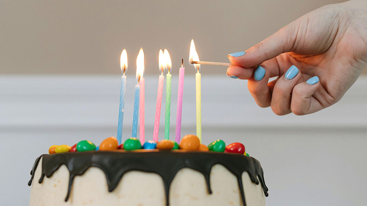 Hand lighting colorful birthday candles on cake with chocolate frosting and candy decorations for sisteru2019s birthday celebration.