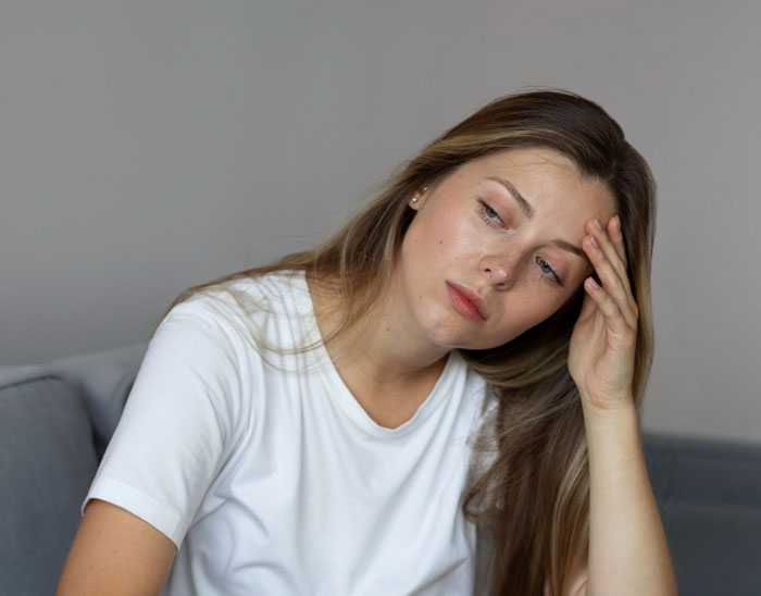Tired woman in a white shirt looking stressed while babysitting, representing a babysitting nightmare scenario.