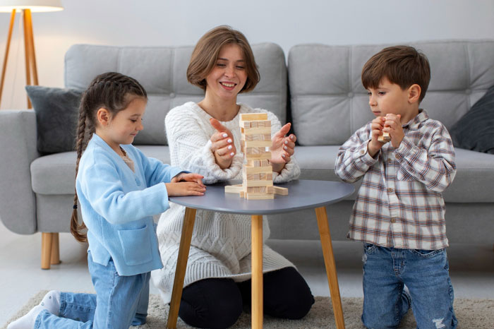 Aunt babysitting kids playing a block game at home, enjoying time while managing a challenging babysitting situation.