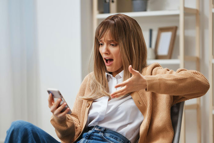 A shocked woman sitting indoors, looking at her phone, reacting to a babysitting nightmare involving SIL’s kids. A shocked woman sitting indoors, looking at her phone, reacting to a babysitting nightmare involving SIL’s kids.