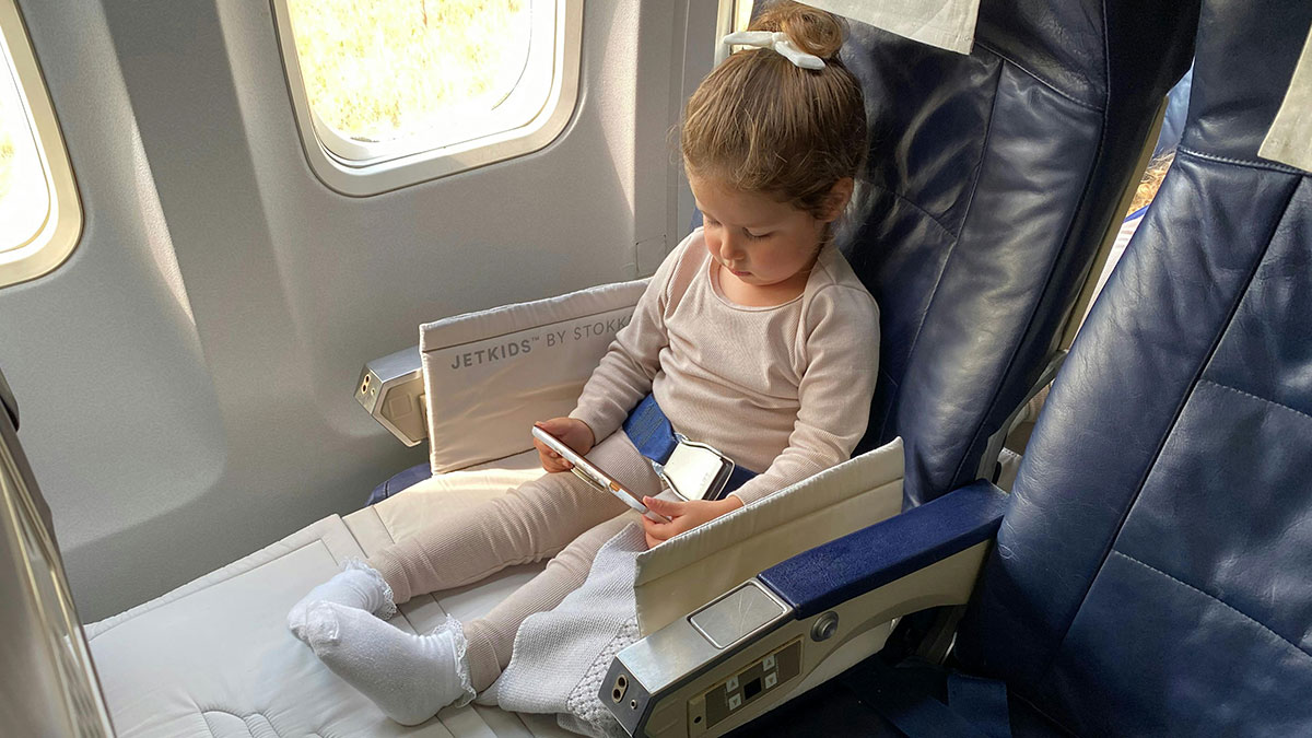 Young child sitting with JetKids seat extender on flight, highlighting passenger moves seats after special needs kid's kickfest.