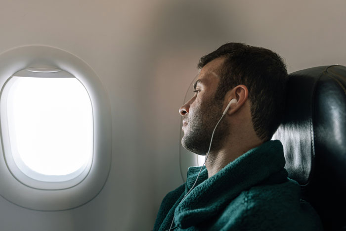 Passenger moves seats on flight, wearing earphones, looking out airplane window, affected by nearby special needs kid's kickfest. Passenger moves seats on flight, wearing earphones, looking out airplane window, affected by nearby special needs kid's kickfest.