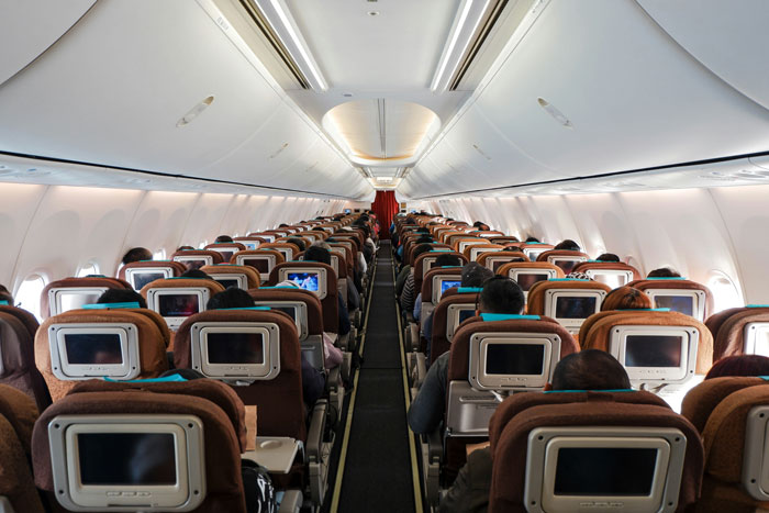 Inside of a commercial flight cabin showing passengers seated during a flight with seatback entertainment screens active. Inside of a commercial flight cabin showing passengers seated during a flight with seatback entertainment screens active.
