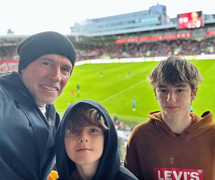 Scott Galloway wearing a black beanie and two boys at a stadium, illustrating the money rules behind Scott Galloway’s net worth.