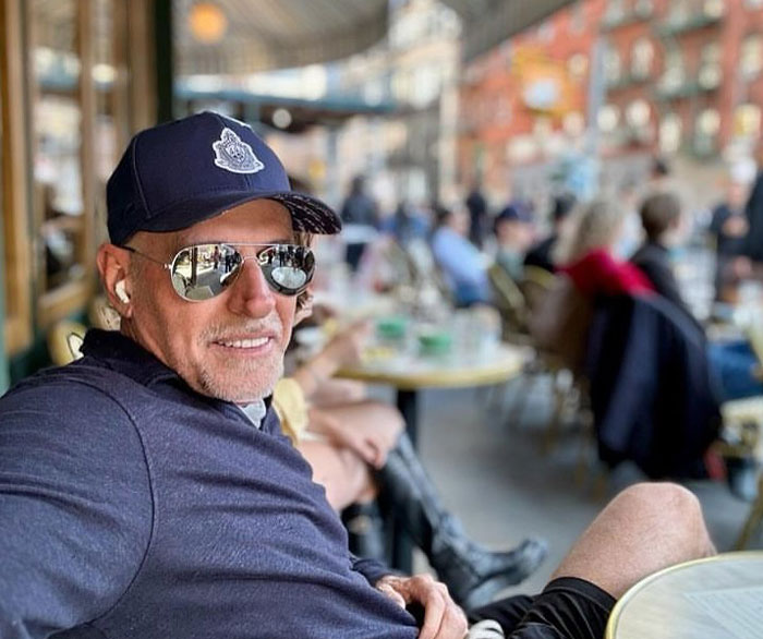 Scott Galloway in sunglasses and cap relaxing at outdoor cafe, representing money rules that drive Scott Galloway net worth.