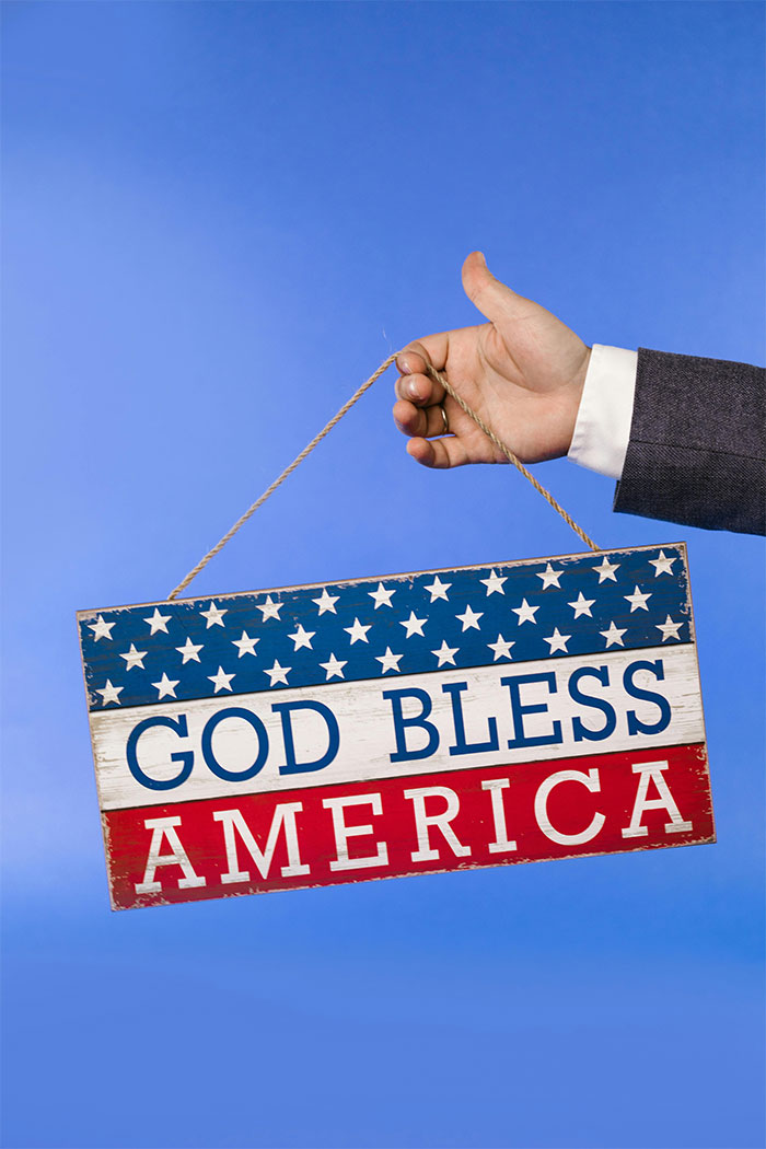 Hand in suit holding a vintage American flag sign with stars and stripes, symbolizing money rules and net worth.