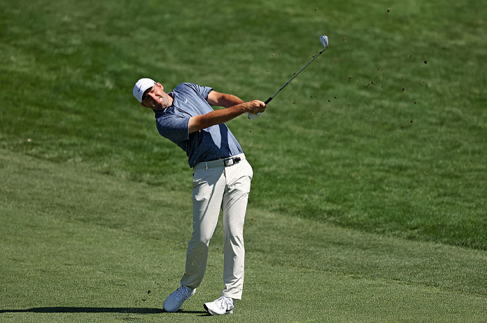 Golfer Scottie Scheffler in mid-swing on a green golf course showcasing golf’s financial power and success.