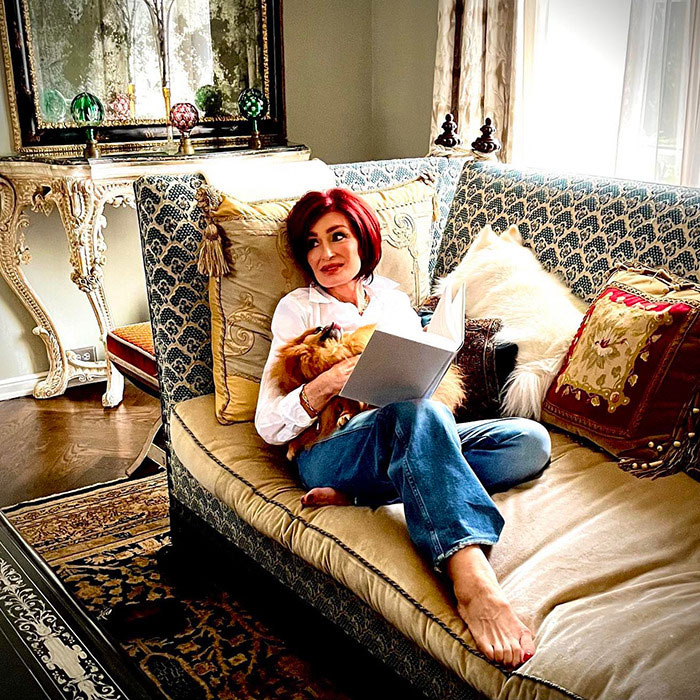 Sharon Osbourne relaxing on a patterned couch, holding a dog and reading a book, showcasing her appearance after using Ozempic. Sharon Osbourne relaxing on a patterned couch, holding a dog and reading a book, showcasing her appearance after using Ozempic.
