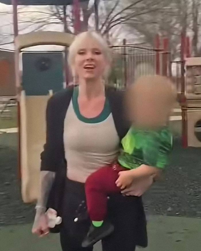 Woman at playground holding child with blurred face, related to trad-wife influencer defending white mom fundraiser controversy. Woman at playground holding child with blurred face, related to trad-wife influencer defending white mom fundraiser controversy.