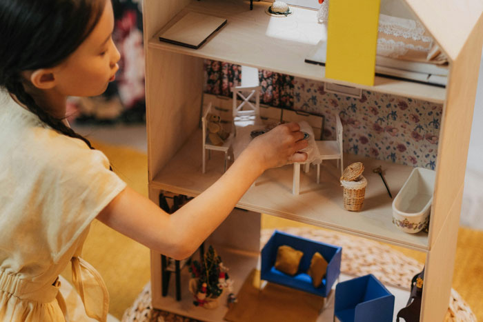 Young girl playing with a dollhouse on her 11th birthday while visiting relatives demand cake, gifts, and attention