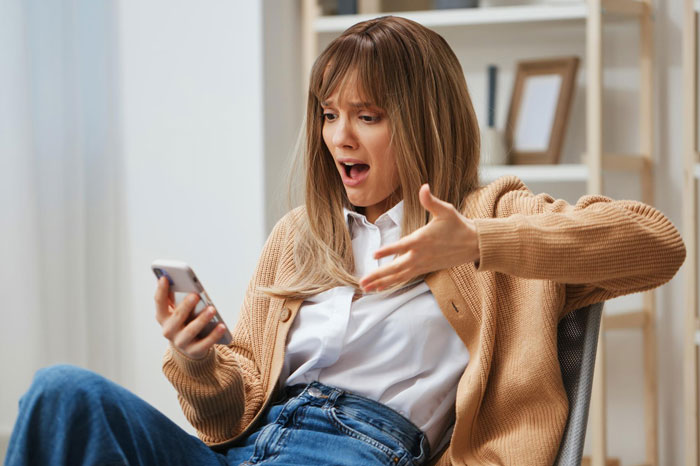 Woman in casual clothes looking shocked at phone, reacting as girl's 11th birthday turns sour with demands for cake and gifts