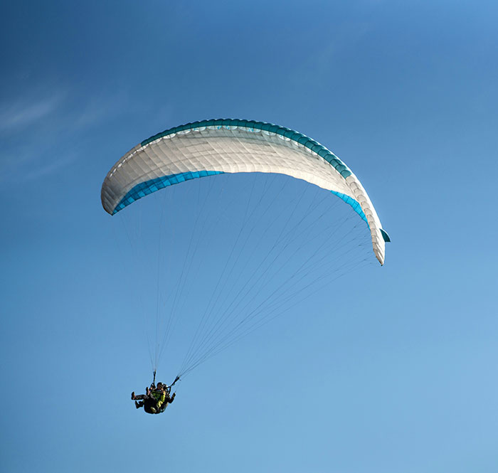 Experienced skydiver with over 400 flights descending under a parachute against a clear blue sky. Experienced skydiver with over 400 flights descending under a parachute against a clear blue sky.