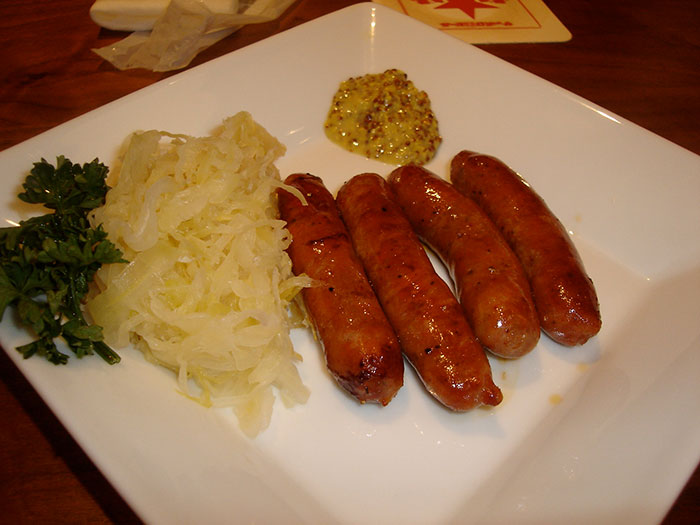 Plate of grilled sausages with sauerkraut, mustard, and parsley representing national stereotypes in food.