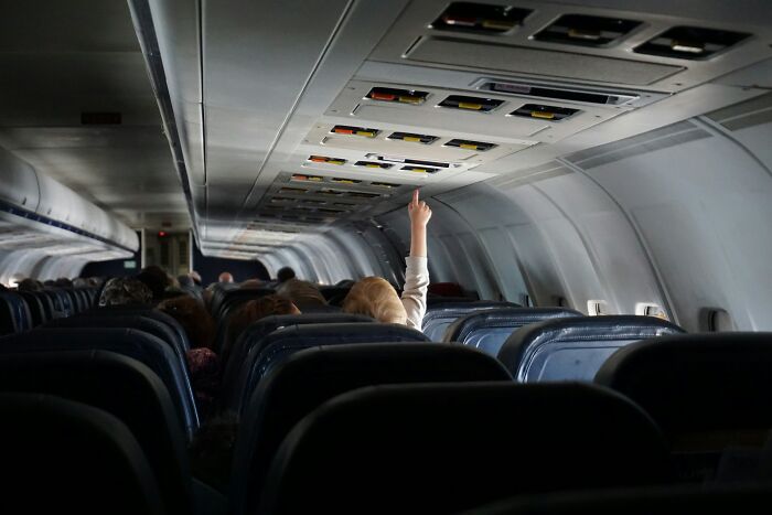 Passenger raising hand inside airplane cabin with common passenger habits annoying flight attendants visible.