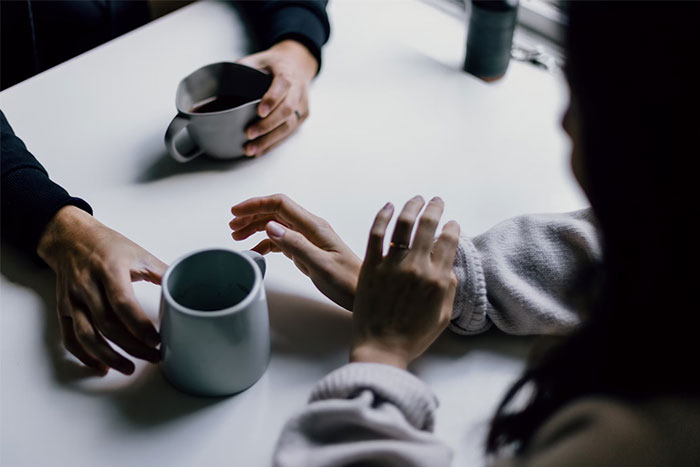Two people talking over coffee, one reaching out as if to stop a proposal during a wedding conversation. Two people talking over coffee, one reaching out as if to stop a proposal during a wedding conversation.