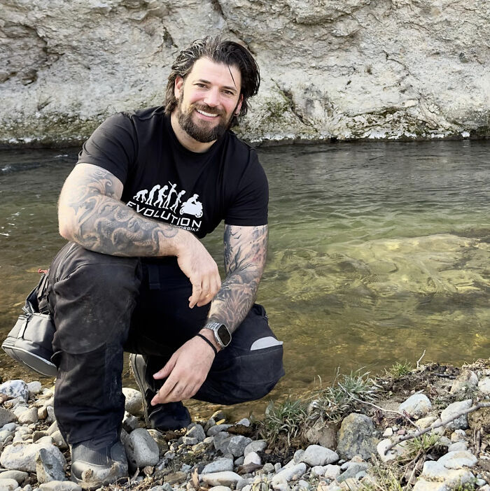 Actor known for playing Viktor Krum in Harry Potter crouching by a riverbank with tattoos on his arms and smiling Actor known for playing Viktor Krum in Harry Potter crouching by a riverbank with tattoos on his arms and smiling