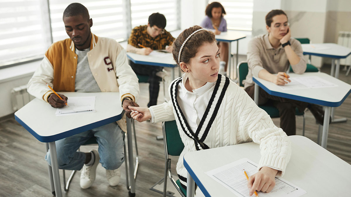 Student caught cheating during quiz, teacher monitors as multiple versions of the same quiz are handed out in classroom.