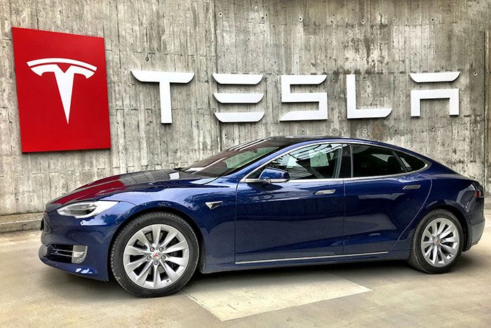 Blue Tesla car parked in front of concrete wall with large Tesla logo, symbolizing Tesla CEO search. Blue Tesla car parked in front of concrete wall with large Tesla logo, symbolizing Tesla CEO search.