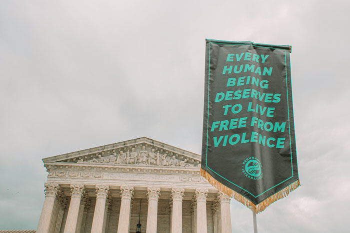 Banner reading every human being deserves to live free from violence held outside a government building highlighting misogyny issues. Banner reading every human being deserves to live free from violence held outside a government building highlighting misogyny issues.