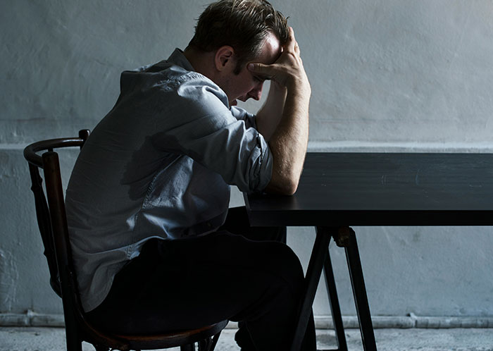 Man sitting at a table with head in hands, illustrating stress from things that could destroy people’s lives quickly.