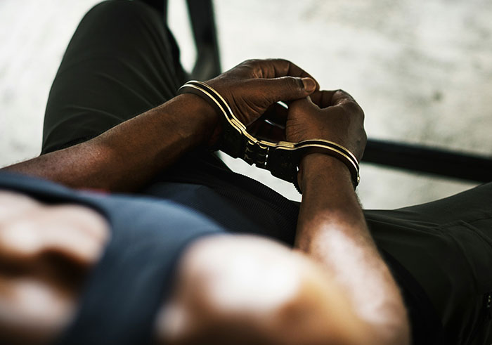 Man with handcuffs on wrists sitting down, illustrating sudden events that could completely destroy people’s lives.