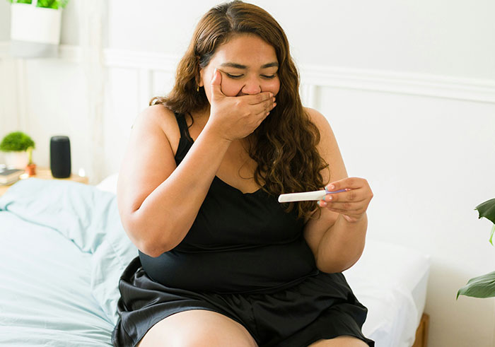 Woman on a bed reacting with shock to a pregnancy test, illustrating things that could completely destroy people’s lives in seconds