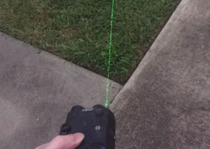 Hand holding a laser pointer aimed at a sidewalk and grass, illustrating risks that could destroy people’s lives quickly.