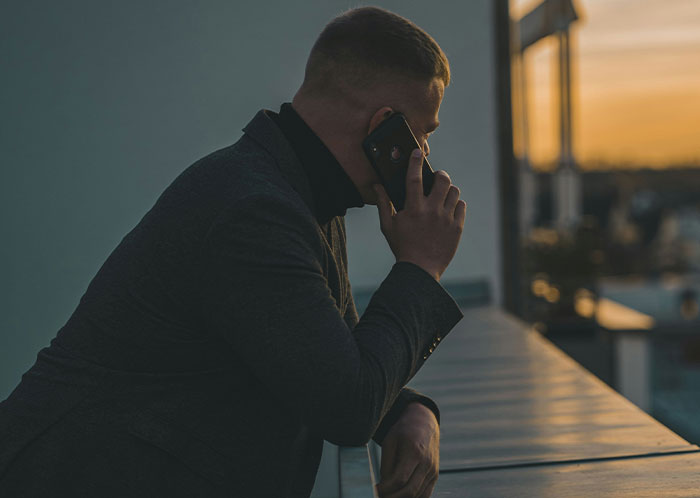 Man in dark coat making a phone call outdoors at sunset, conveying stress related to things that could destroy lives.
