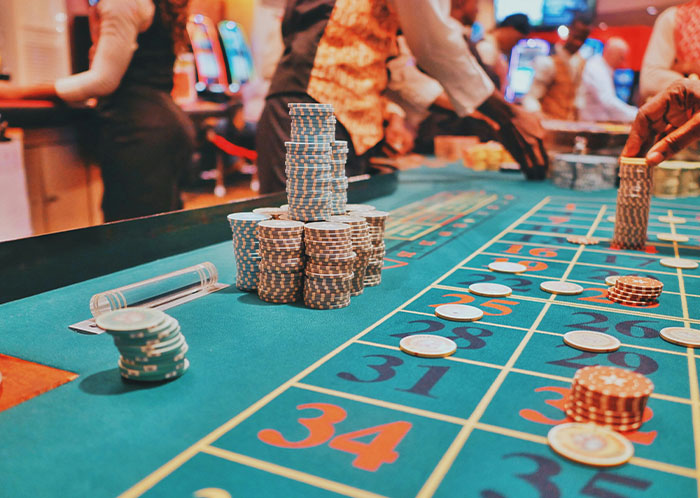 Stacked casino chips on a roulette table with dealers handling chips, illustrating risks that could destroy people’s lives.