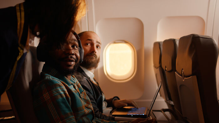 Two passengers seated on a plane looking at a flight attendant, illustrating common passenger habits annoying flight attendants. Two passengers seated on a plane looking at a flight attendant, illustrating common passenger habits annoying flight attendants.