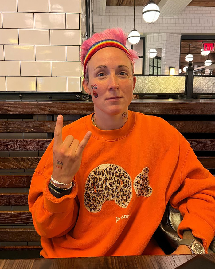 Female athlete with pink hair and orange sweatshirt sitting in a restaurant after restroom mix-up incident. Female athlete with pink hair and orange sweatshirt sitting in a restaurant after restroom mix-up incident.