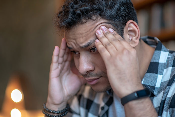 Young man in checkered shirt looking stressed while holding his head, reflecting on cheating evidence found in phone data. Young man in checkered shirt looking stressed while holding his head, reflecting on cheating evidence found in phone data.