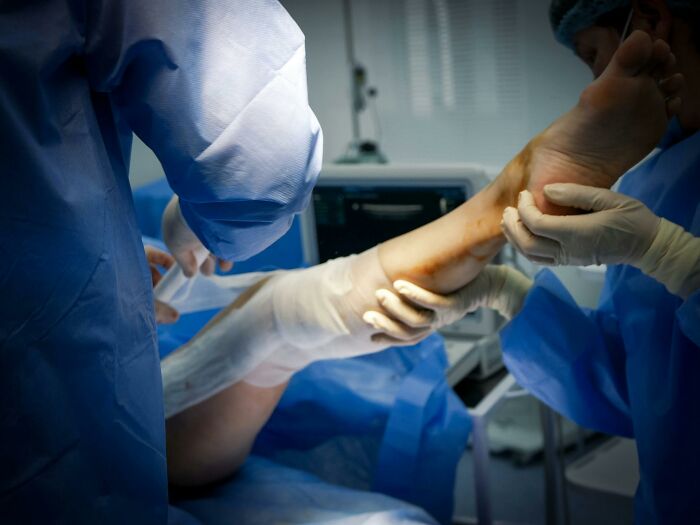 Surgeons in protective gear examining a patient's leg during surgery, highlighting unhealthy human things in medical care.