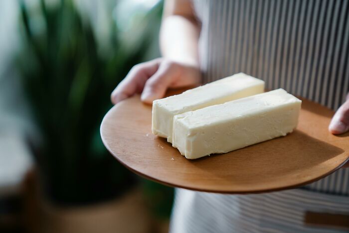 Person holding a wooden plate with two sticks of butter, highlighting unhealthy human things related to diet.