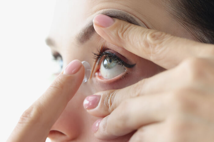 Close-up of a person inserting a contact lens, illustrating unhealthy human things related to eye care habits.