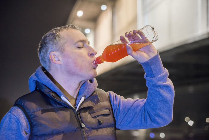 Man drinking sugary soda at night, illustrating one of the unhealthy human things linked to poor diet habits.